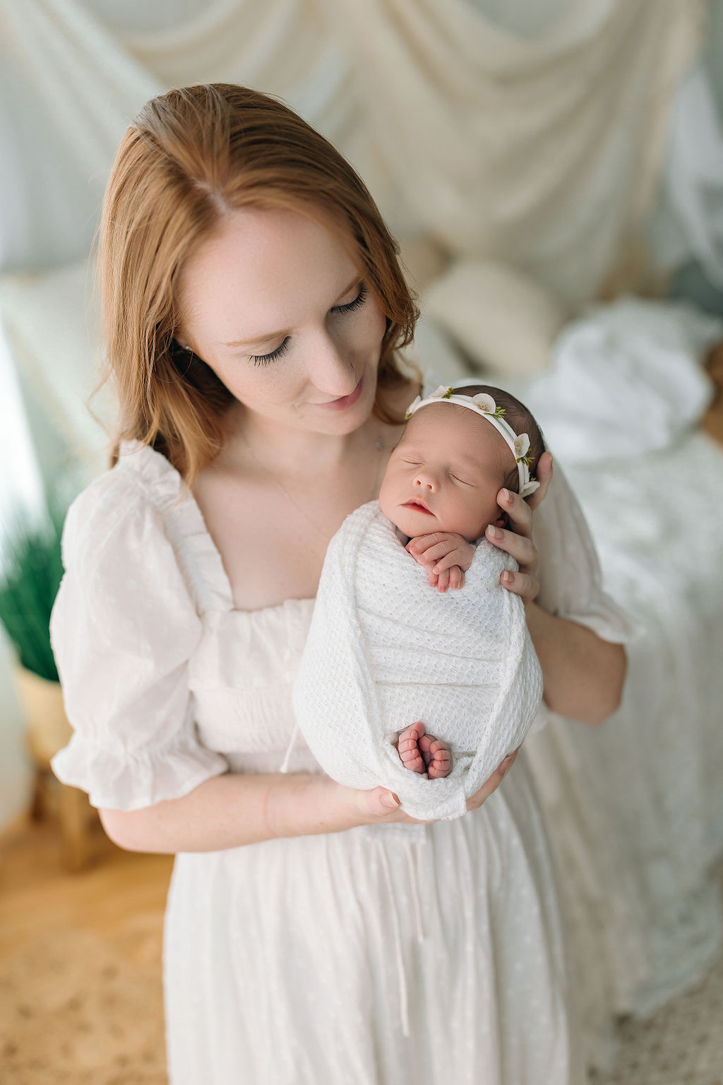 A newborn baby sleeps in mom's hands while she stands in a studio