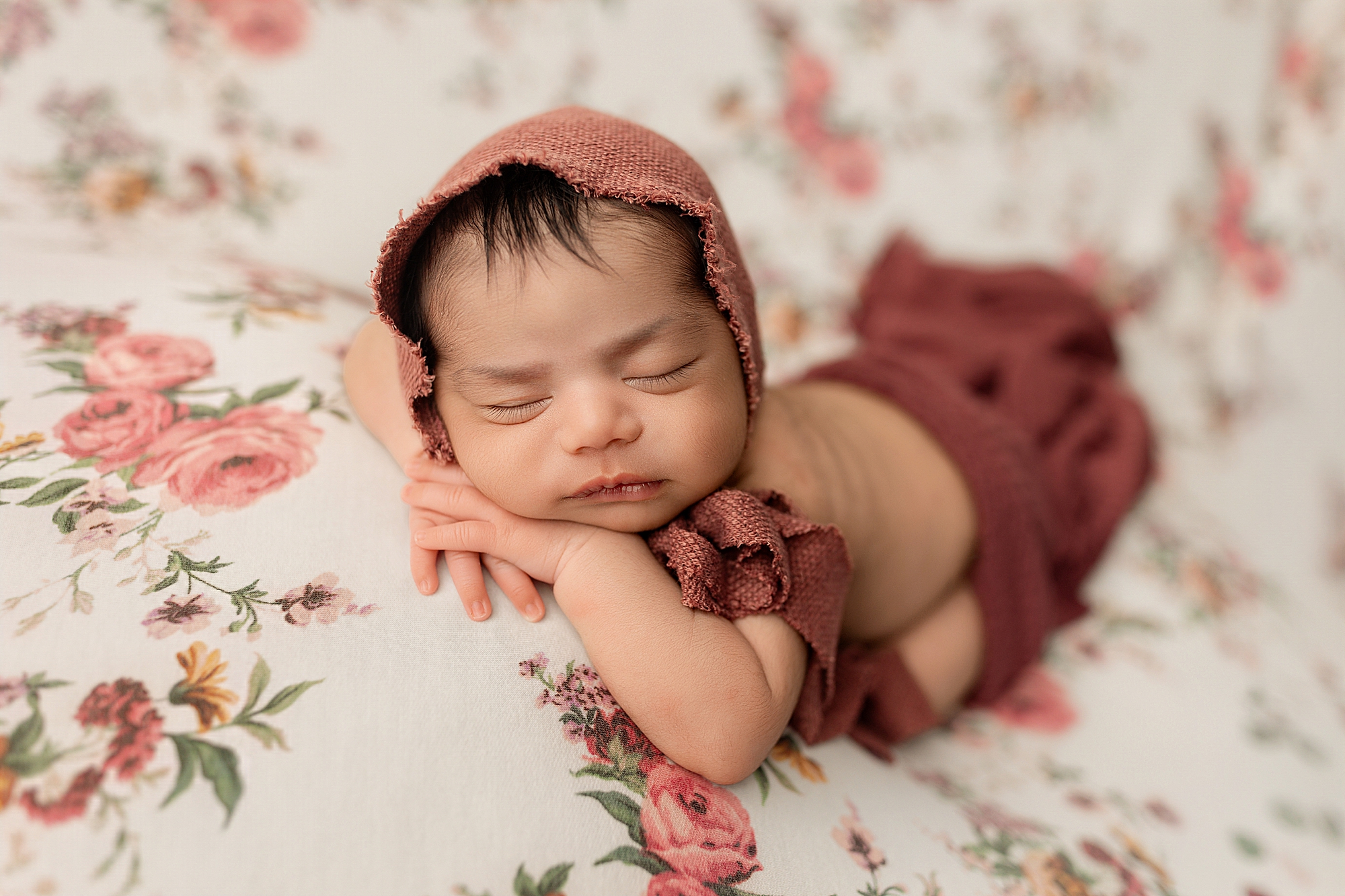 Newborn baby girl on floral backdrop with pink bonnet