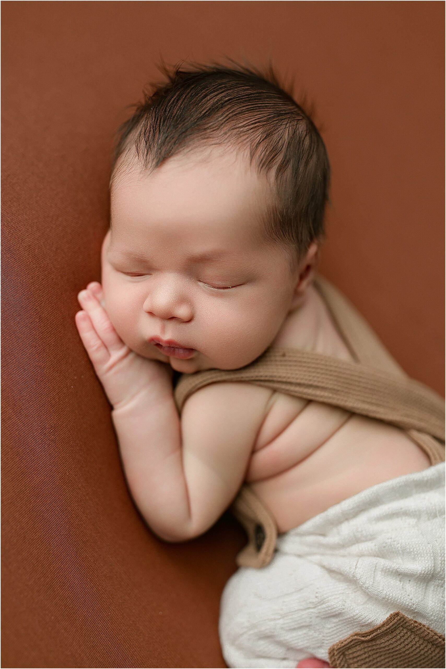Baby boy on brown backdrop wearing suspenders