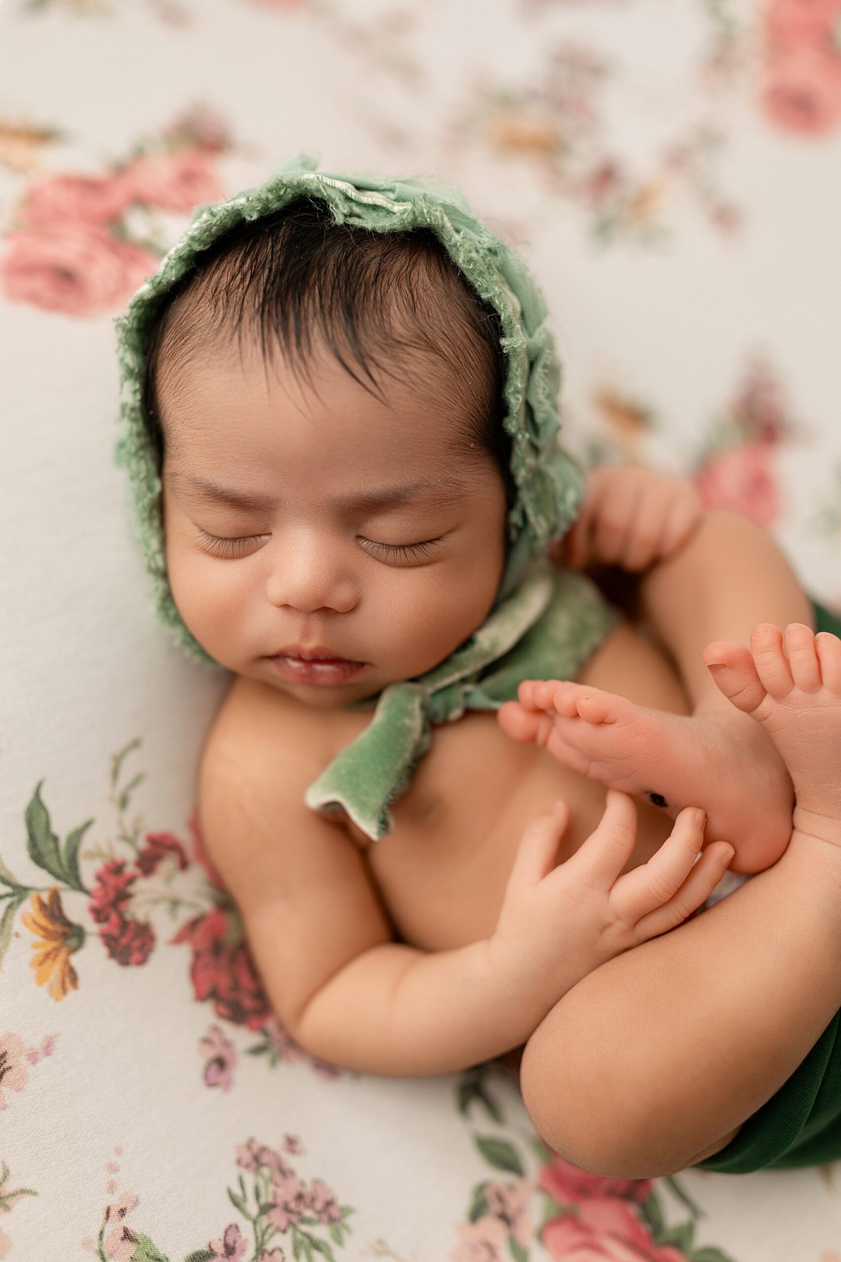 Newborn baby girl on floral backdrop with green bonnet