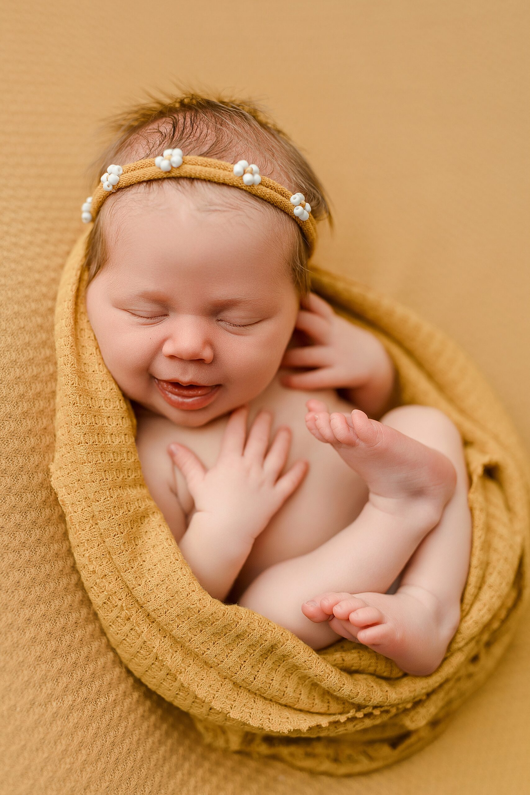 Newborn baby girl smiling with yellow backdrop