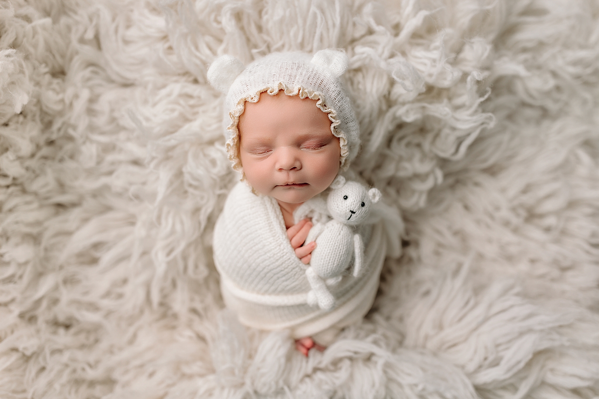 Baby girl in white holding tiny teddy bear