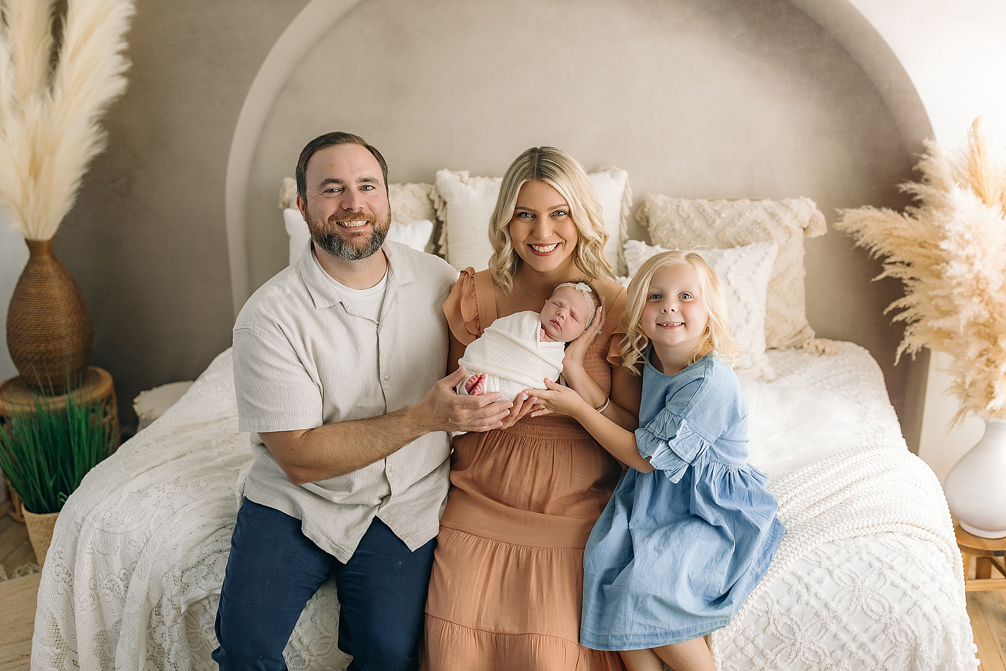 Family sitting on bed in newborn studio holding baby