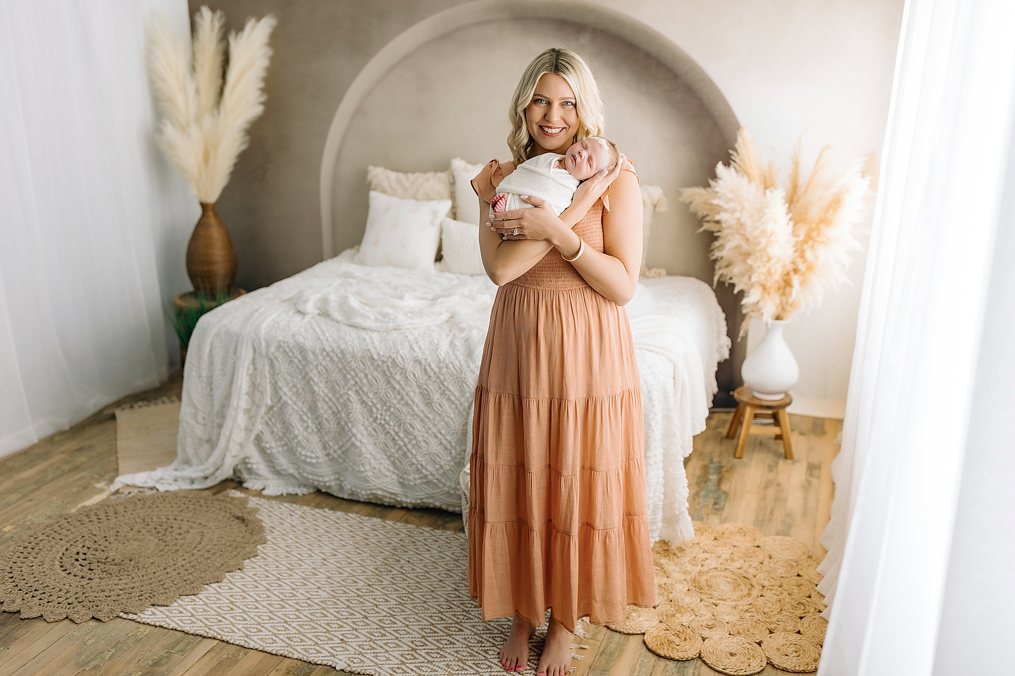 Mom holding newborn baby girl wrapped in white in photography studio