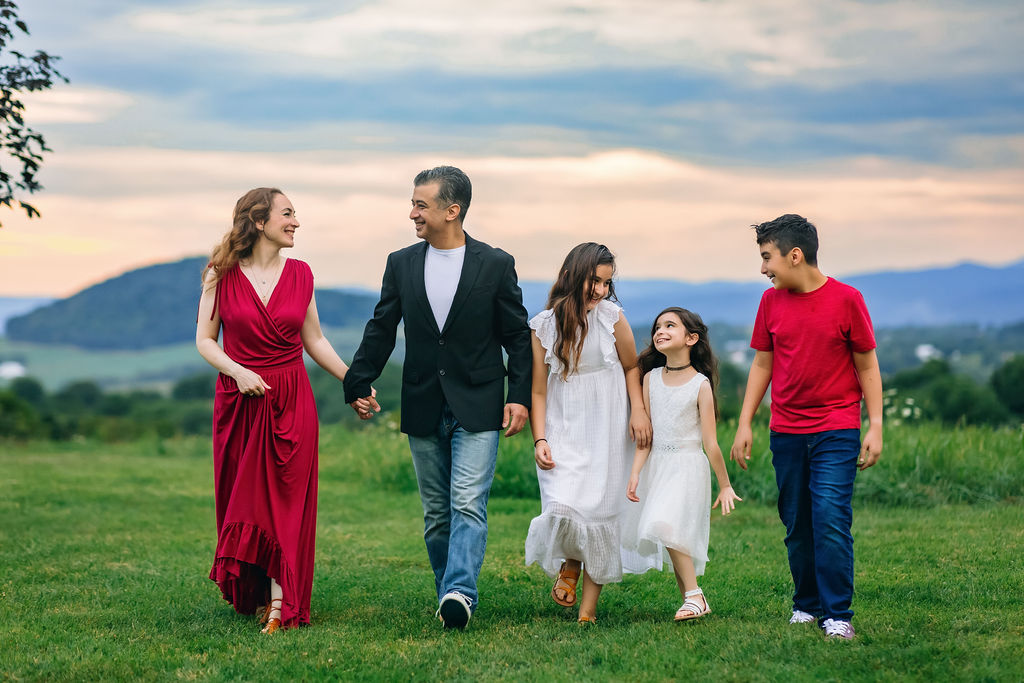 A family of five hold hands and walk together through a field at sunset charlottesville waldorf school
