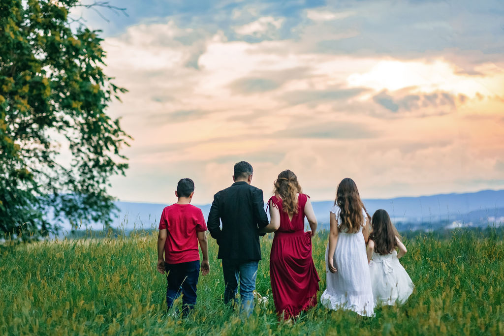 A family of five walk through tall grass on a hill at sunset charlottesville waldorf school