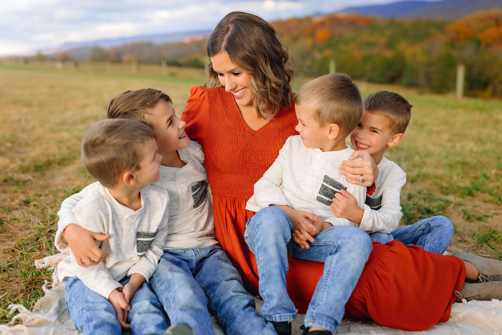 A mom sits on a blanket hugging her four sons in a field explore more discovery museum