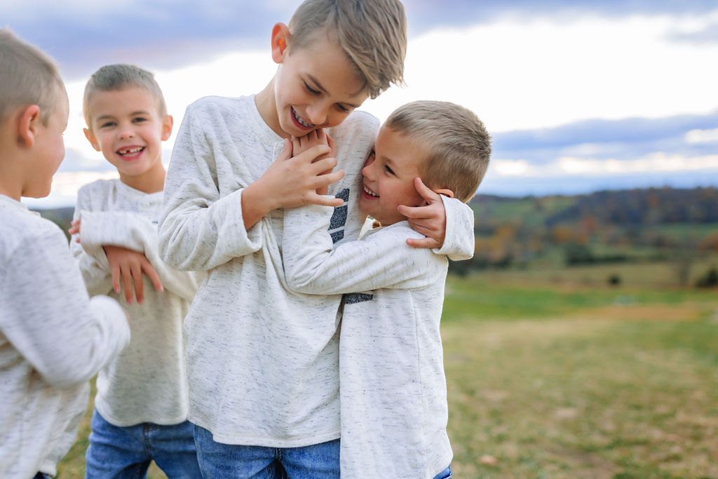 Four young brothers in matching shirts and jeans plays together on a grassy hill explore more discovery museum