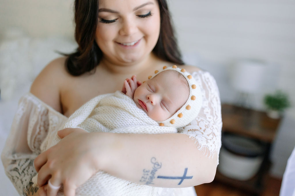 A mom smiles down at her sleeping newborn baby in a knit swaddle and hat lavender lactation