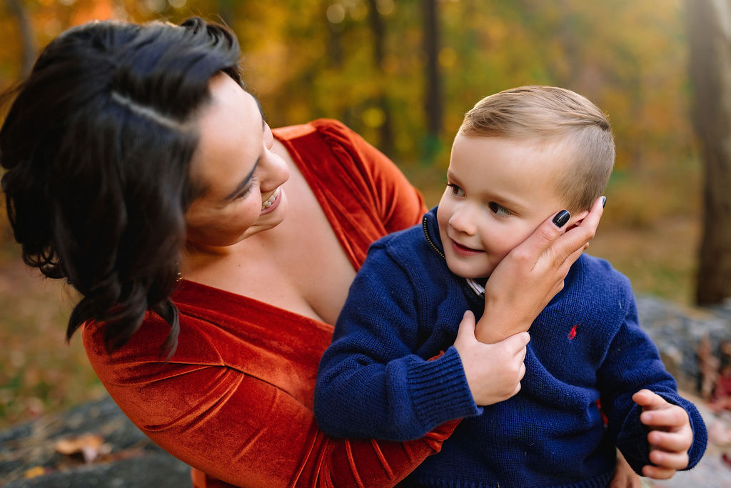 A mother in a velvet dress holds and plays with her young son in a blue sweater montessori preschool charlottesville