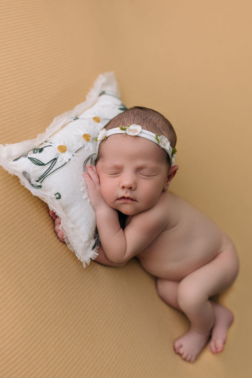 A newborn baby sleeps naked on a white daisy pillow monticello nannies