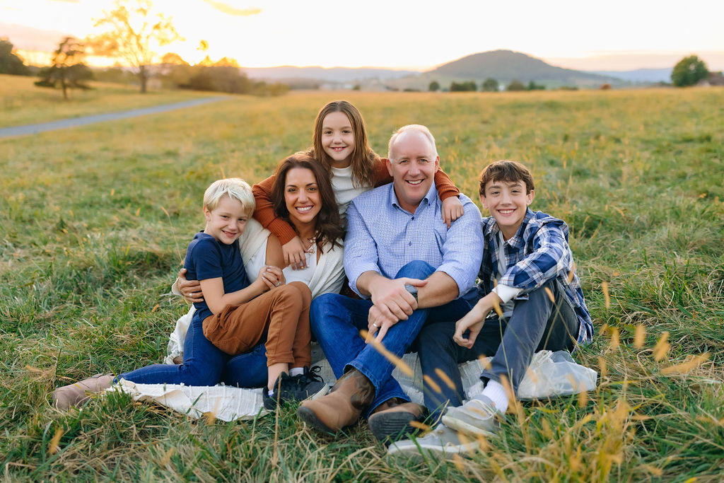 A family of five sit on a picnic blanket in a grassy field at sunset virginia discovery museum