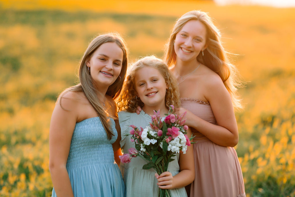 Three sisters hug while picking wildflowers at sunset