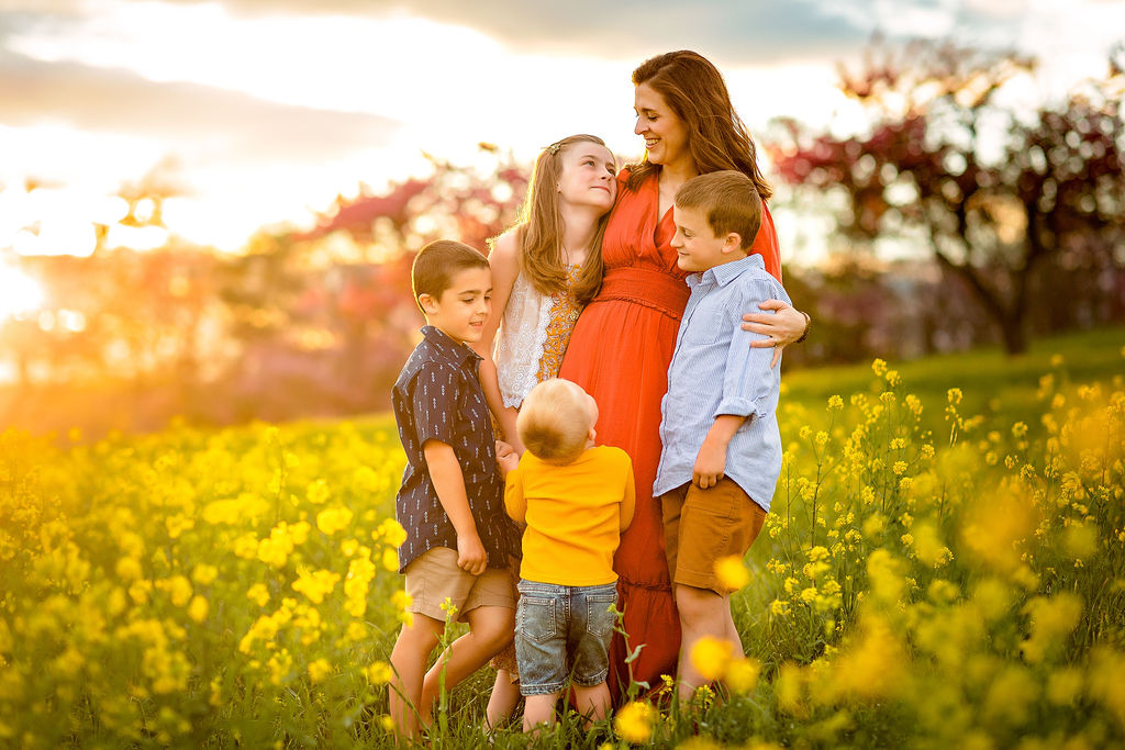 A mother in a red dress stands in a field of yellow wildflowers while hugging her four children fall activities shenandoah valley