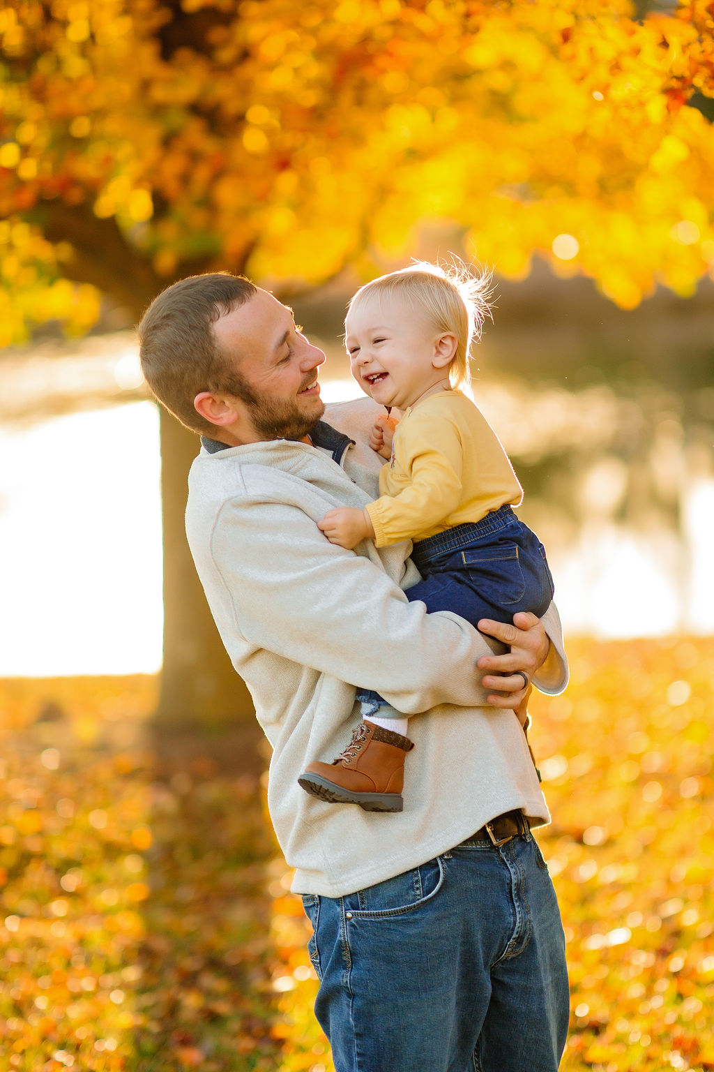 A father laughs and plays with his toddler daughter in a yellow shirt in a park in fall