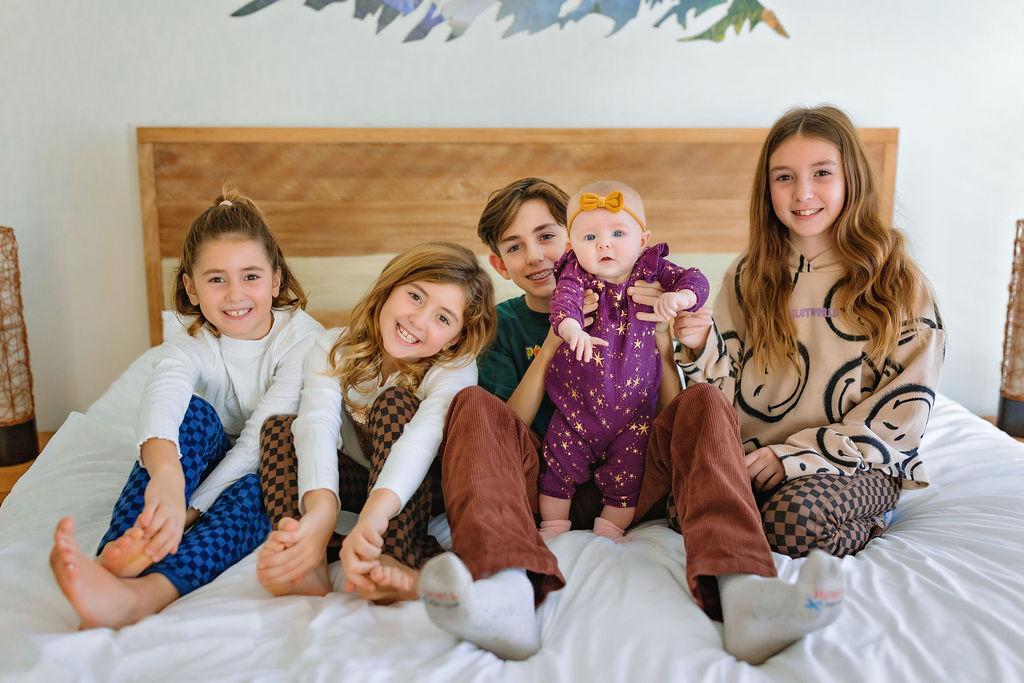 Five siblings sit on a white bed together in while wearing matching pajamas before visiting winchester christmas events