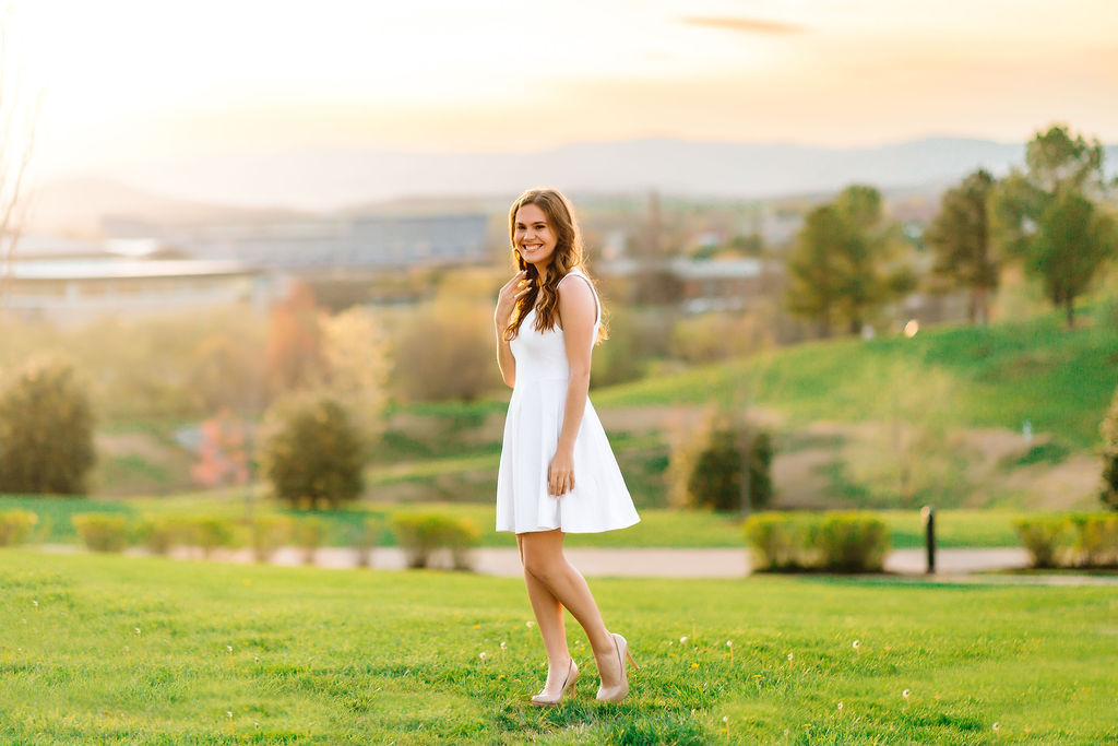 A college grad completes her jmu bucket list while walking on a grassy hill in a white dress