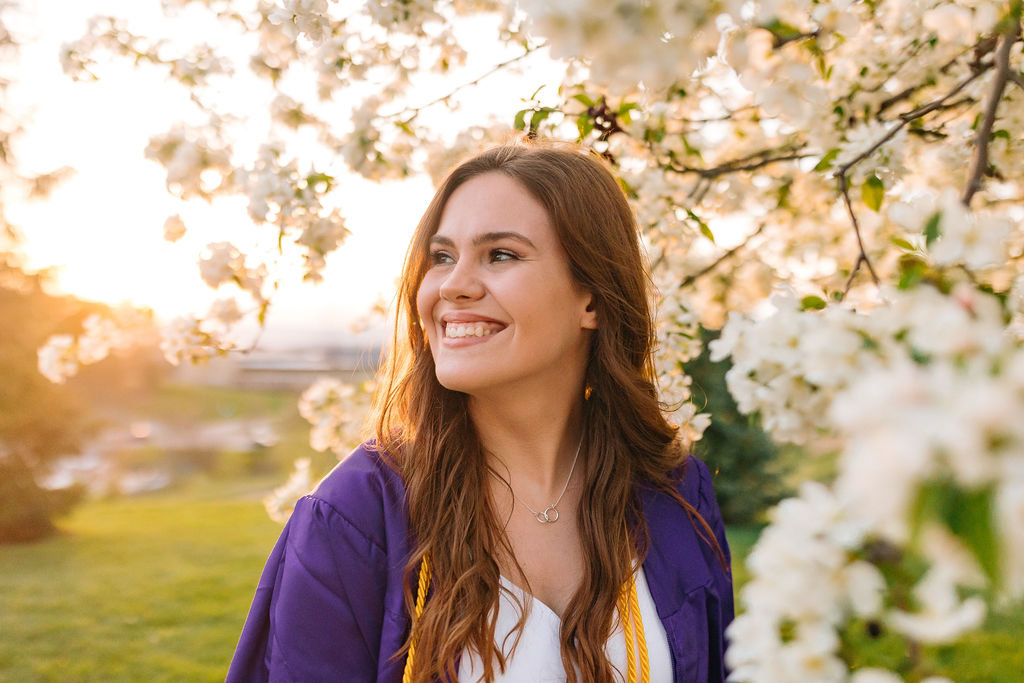 A college grad stands among a flowering tree smiling at sunset after benefiting from jmu dual enrollment