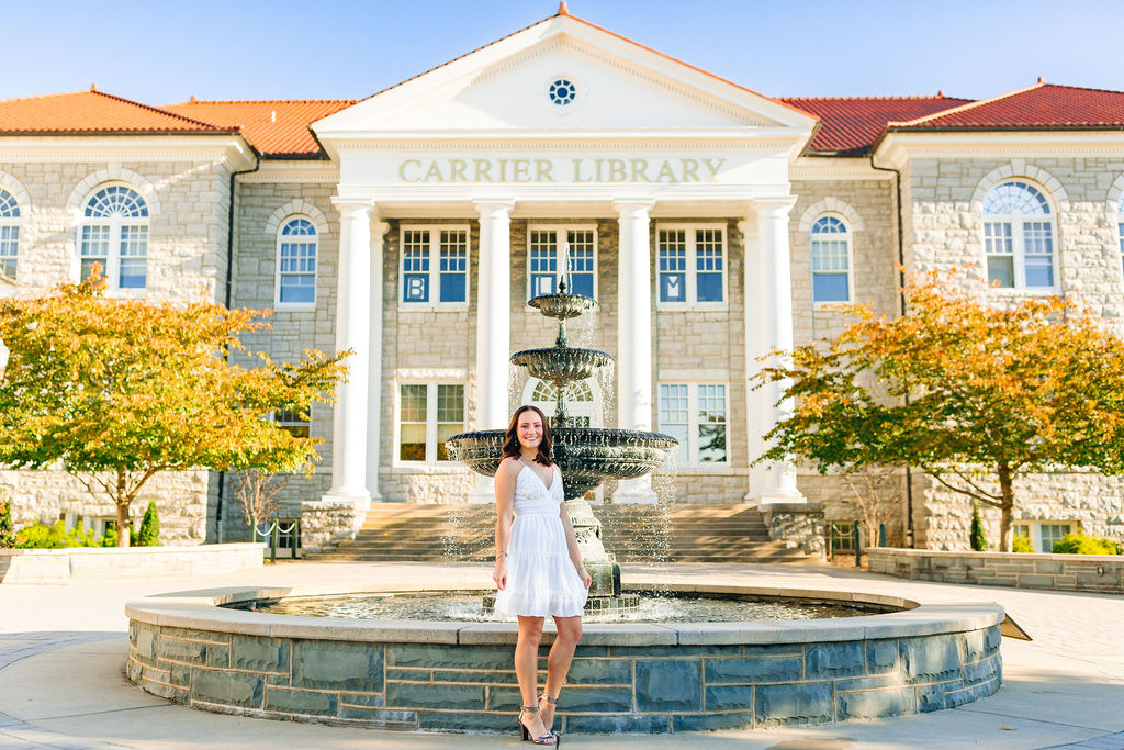 A JMU grad stands in front of the library fountain in a white dress