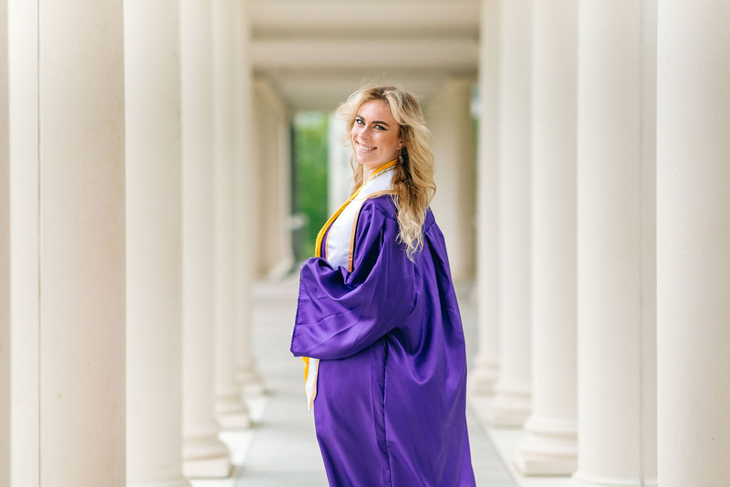 A college graduate in a purple robe looks over her shoulder while walking through columns
