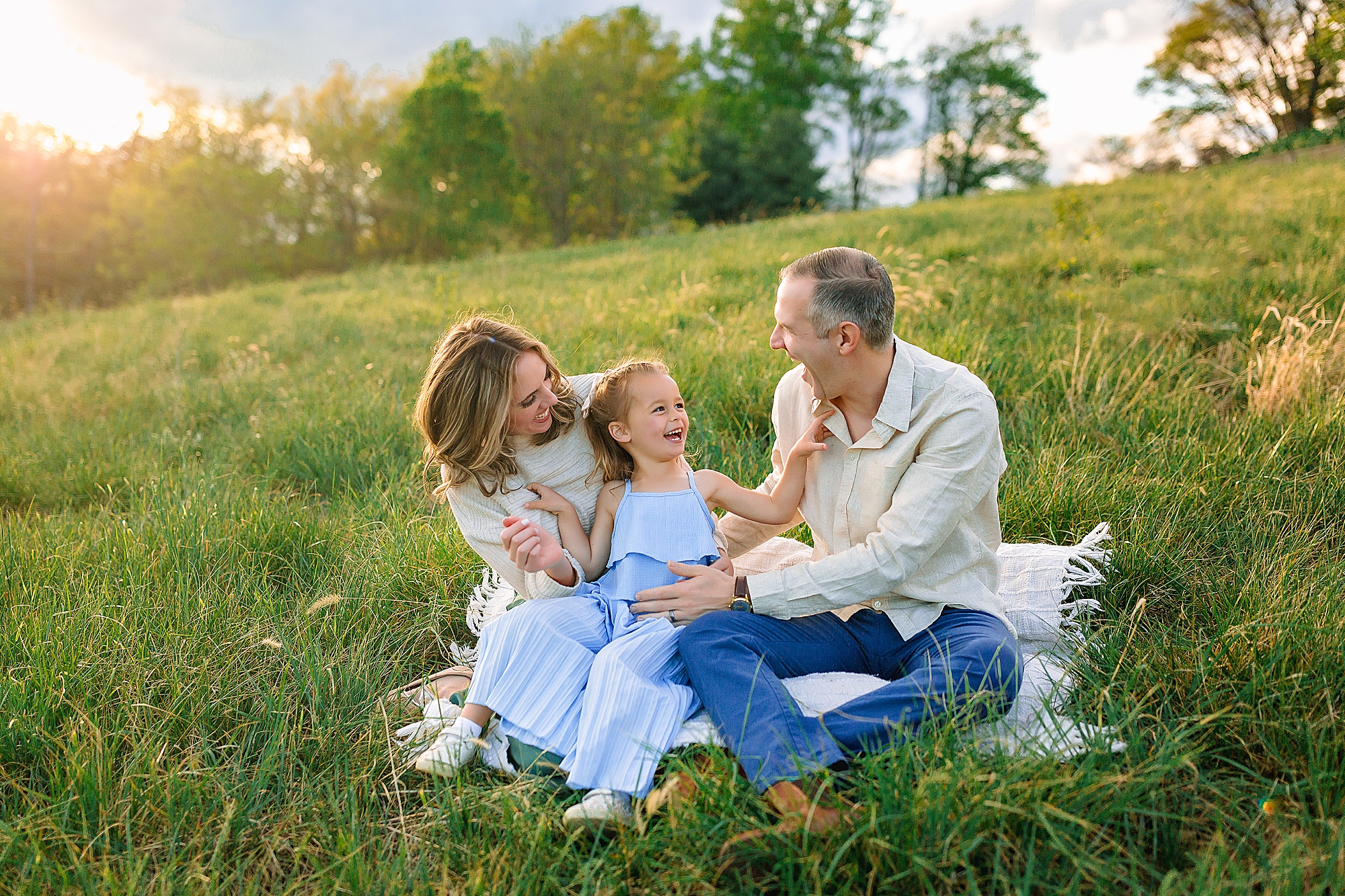 Family sitting on a blanket in a field laughing in Harrisonburg, VA